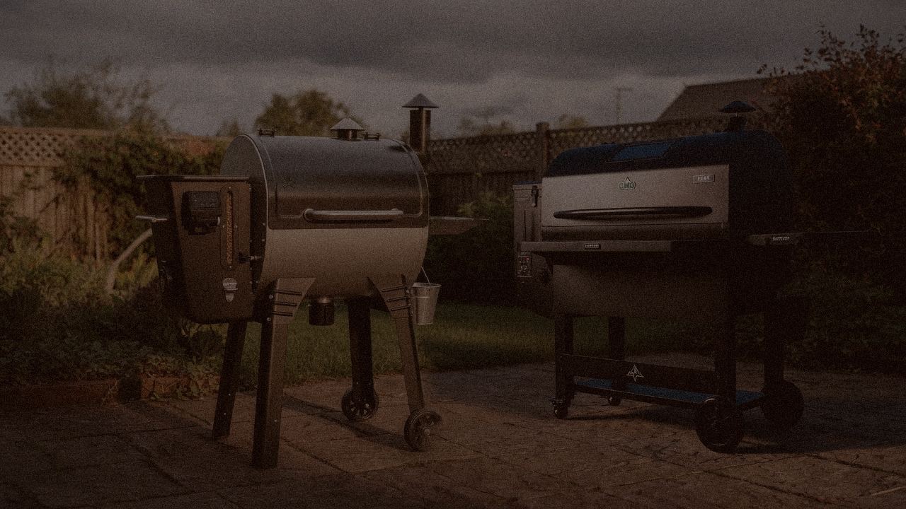 Camp Chef Woodwind WiFi 24 and Green Mountain Grills Peak at night with smoke, wood pellet grills on a dark patio