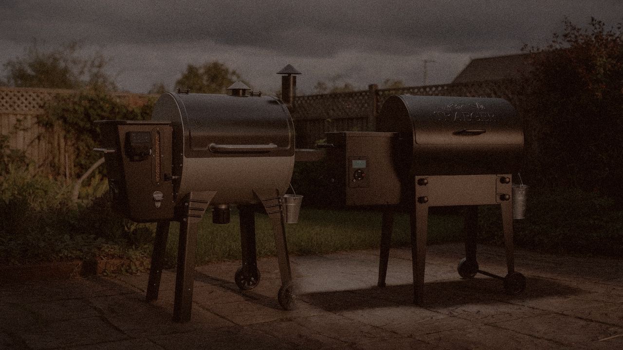 Camp Chef Woodwind WiFi 24 and Traeger Tailgater 20 at night with smoke, wood pellet grills on a dark patio