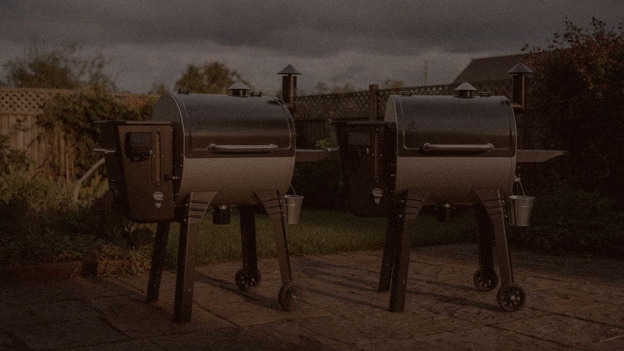 Camp Chef Woodwind Pro WiFi 24 and Camp Chef Woodwind WiFi 24 at night with smoke, wood pellet grills on a dark patio