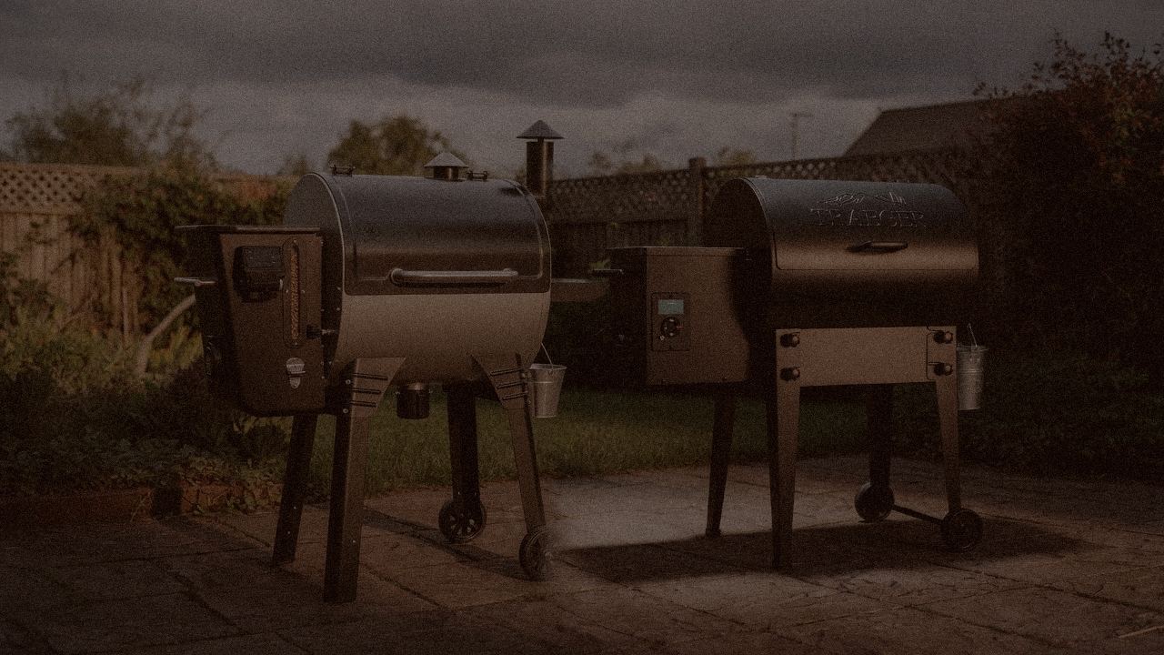 Camp Chef Woodwind Pro WiFi 24 and Traeger Tailgater 20 at night with smoke, wood pellet grills on a dark patio