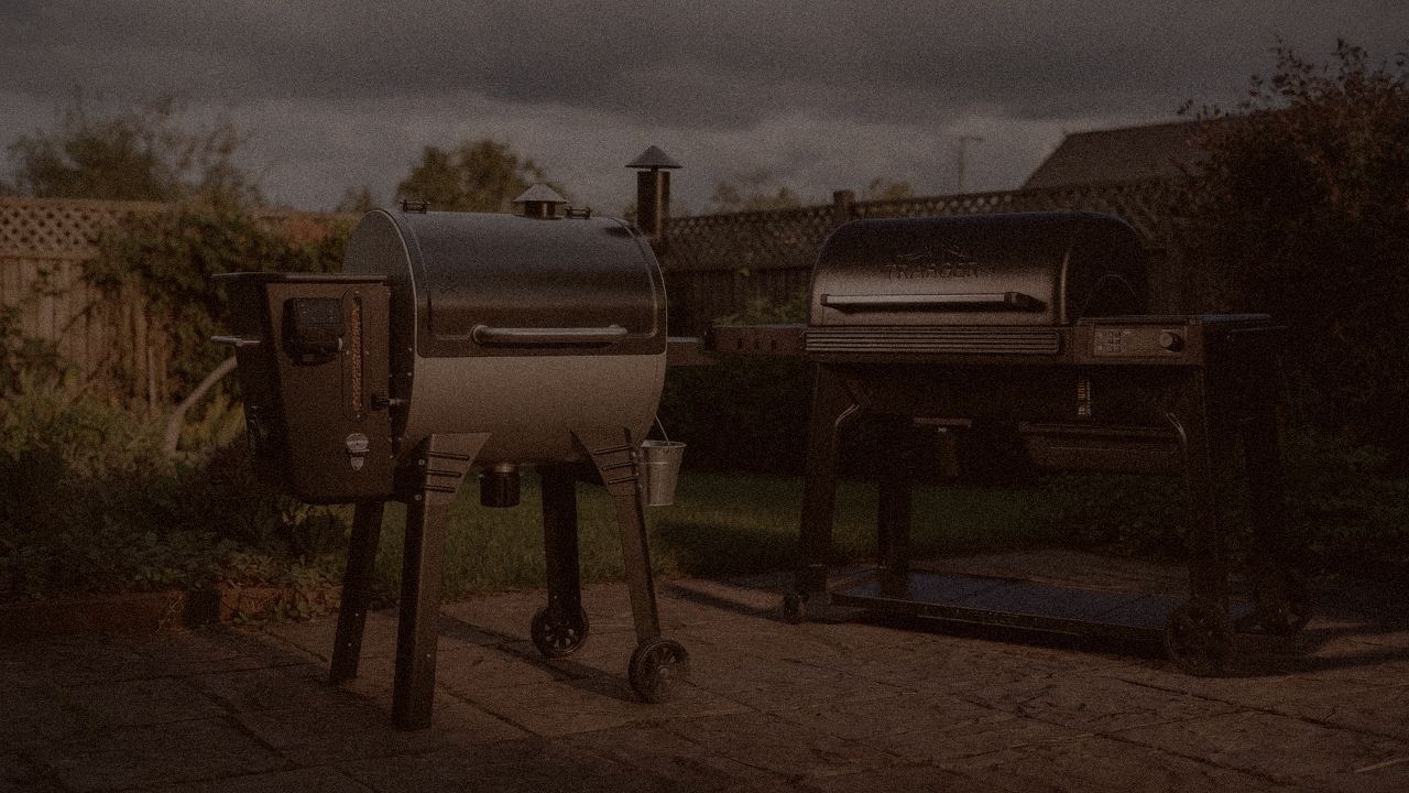 Camp Chef Woodwind Pro WiFi 24 and Traeger Timberline at night with smoke, wood pellet grills on a dark patio
