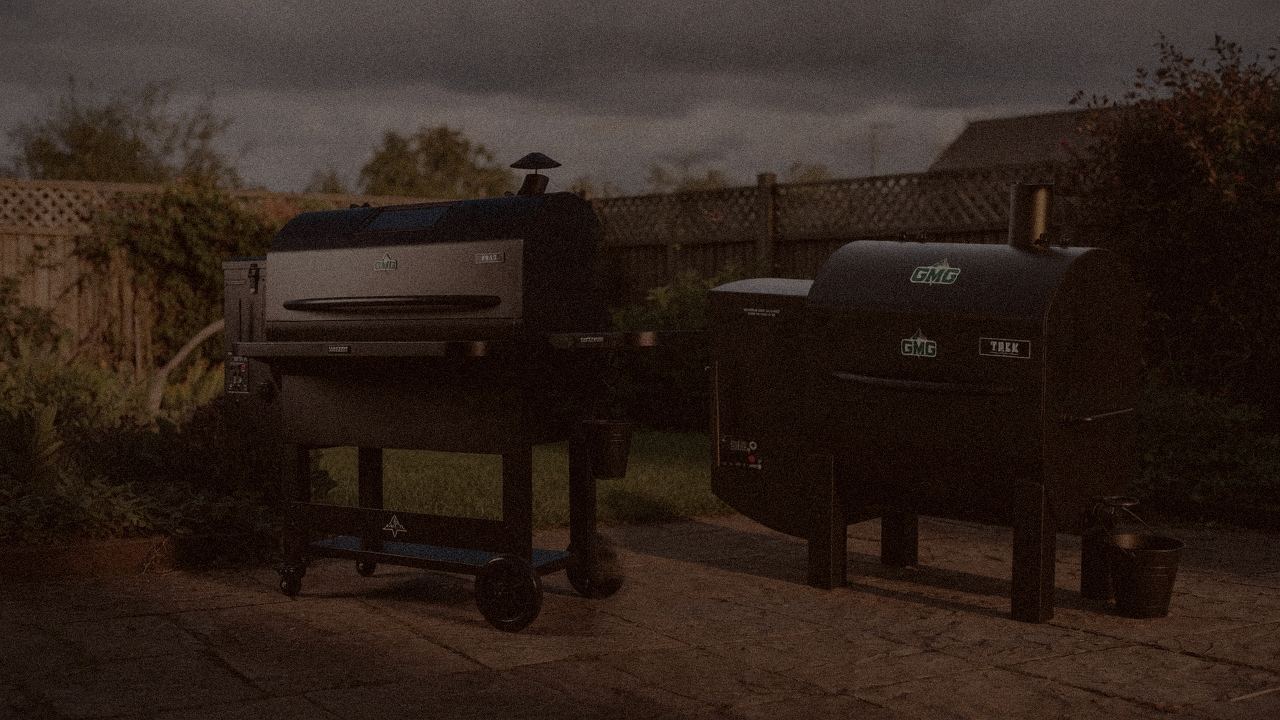 Green Mountain Grills Peak and Green Mountain Grills Trek at night with smoke, wood pellet grills on a dark patio
