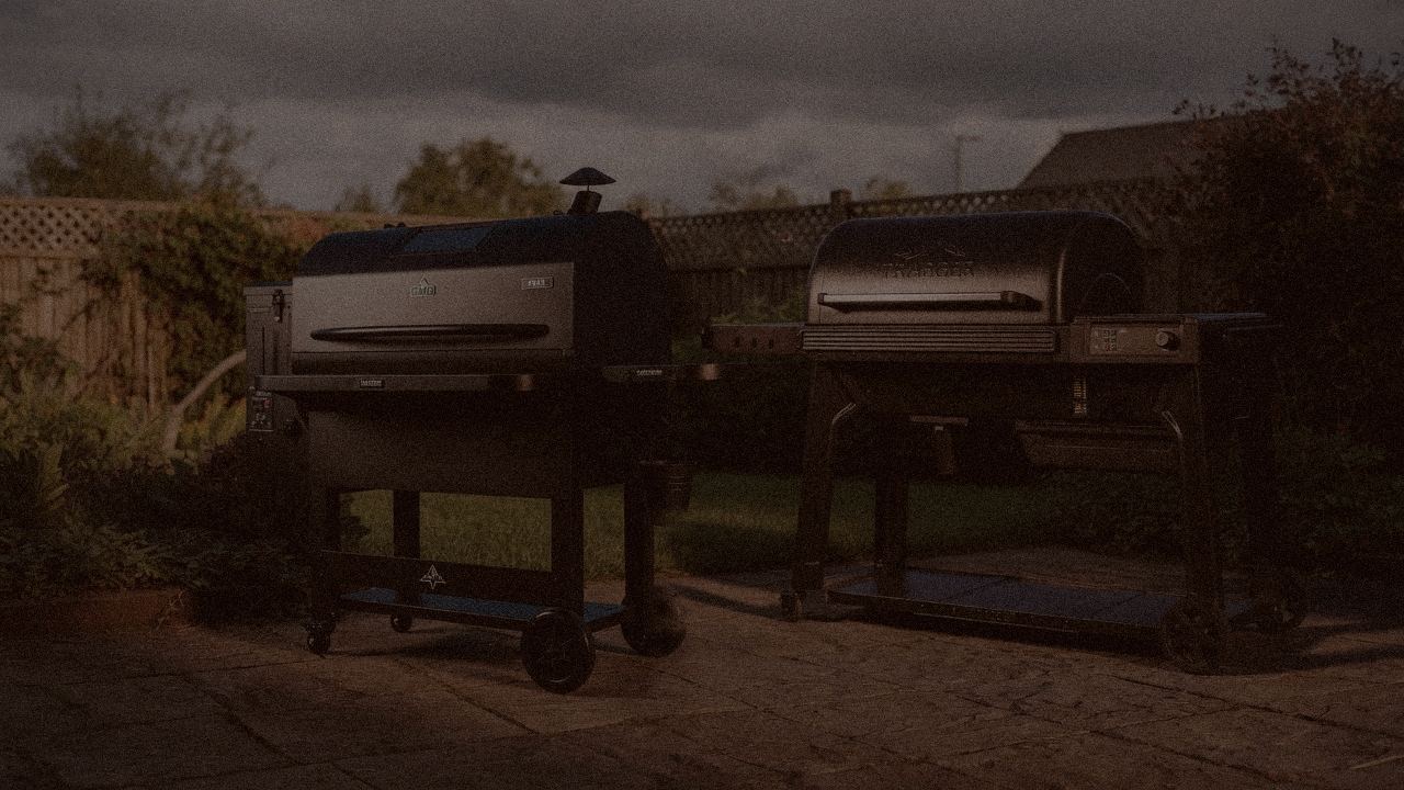 Green Mountain Grills Peak and Traeger Timberline at night with smoke, wood pellet grills on a dark patio