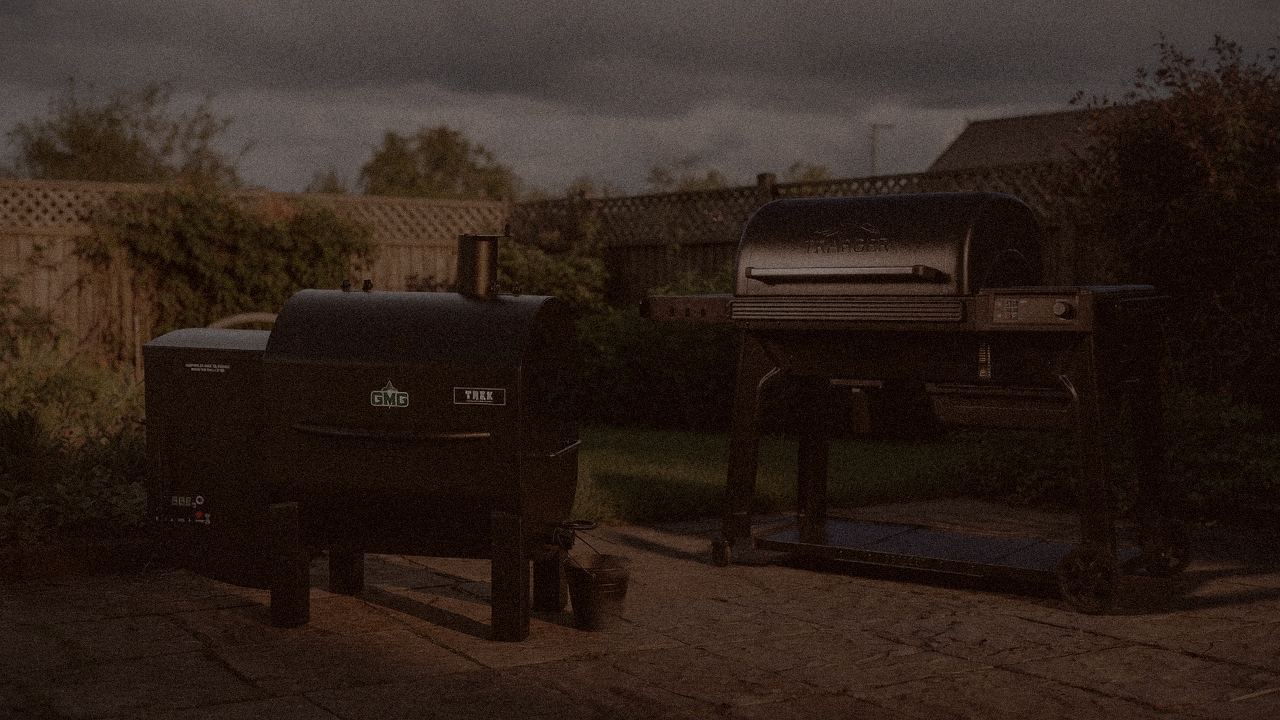 Green Mountain Grills Trek and Traeger Timberline at night with smoke, wood pellet grills on a dark patio