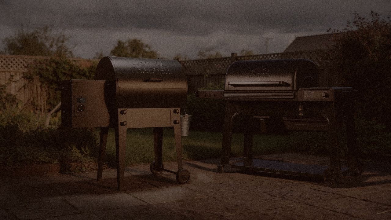 Traeger Tailgater 20 and Traeger Woodridge Pro at night with smoke, wood pellet grills on a dark patio